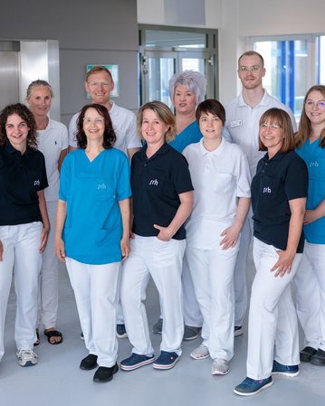 Eine Gruppe von zehn Personen in Arbeitskleidung steht in einem modernen Innenraum, umgeben von Pflanzen und Fenstern.