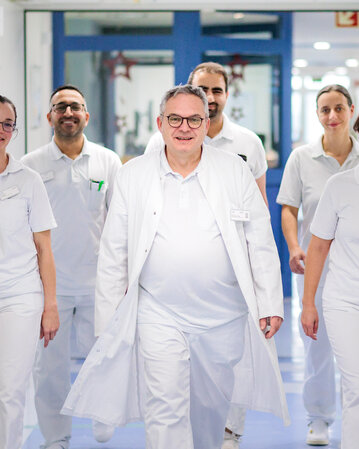 Sechs medizinische Fachkräfte in weißen Kitteln gehen gemeinsam durch einen Krankenhausflur.